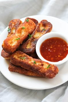 some fried food on a white plate next to a small bowl of sauce and a fork