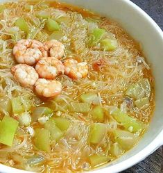 a bowl of soup with shrimp and celery in it on a wooden table