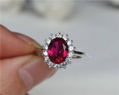 a close up of a person holding a ring with a red stone