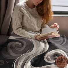 a woman reading a book while sitting on a bed in front of a window with curtains