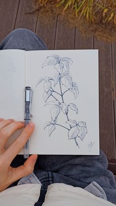 a person holding an open book with a pen in their hand and drawing flowers on it