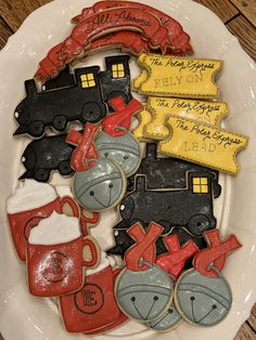 decorated cookies are arranged on a plate with writing in the shape of train tracks and mugs