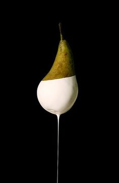 a white spoon with a pear on it and some liquid dripping from the top, against a black background