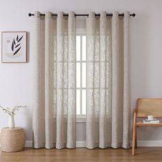 a living room with white walls and wooden flooring, two windows covered in sheer curtains