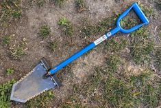 a blue shovel laying on the ground next to some grass and dirt with one end missing