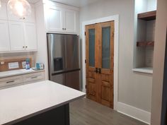 a kitchen with white cabinets, stainless steel refrigerator and an island in front of it