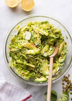 a glass bowl filled with shaved brussels sprouts and sliced lemons next to a wooden spoon