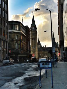 a city street with tall buildings and a clock tower in the distance, on a cloudy day