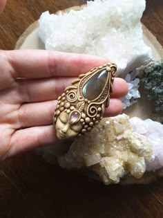 a person holding a ring in their hand near some rocks and other crystals on a table