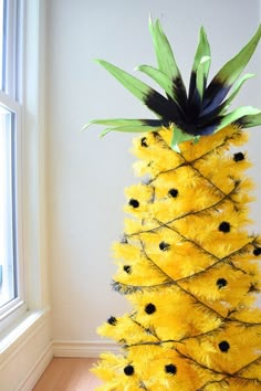 a pineapple decorated with black and yellow feathers on a wooden floor next to a window