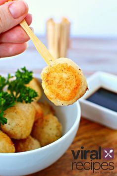 a hand holding a small piece of bread over a bowl of potatoes with parsley