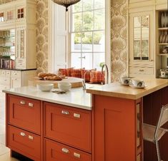 an orange island in a large kitchen with lots of counter space and decor on the walls