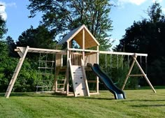 a wooden playset with a slide and swing set in the grass next to trees