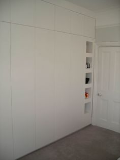 an empty room with white walls and shelving unit in the corner between two doors