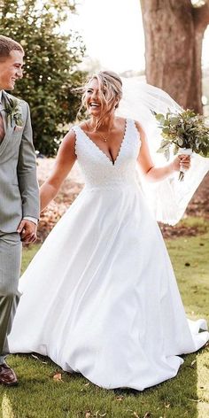 a bride and groom holding hands walking through the grass in front of a large tree