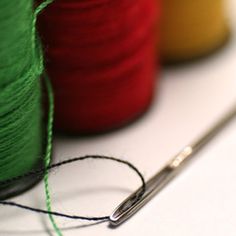 several spools of thread and needle on a white surface with two colors of yarn