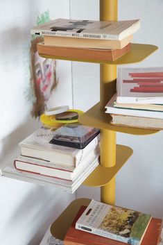 three tiered bookshelf with magazines stacked on each other in front of a white wall