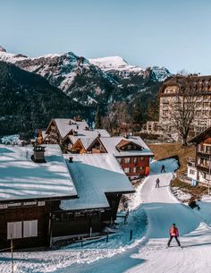 a person riding skis down a snow covered slope next to buildings and mountain range