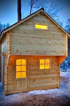 a small wooden cabin in the snow with windows lit up on it's side