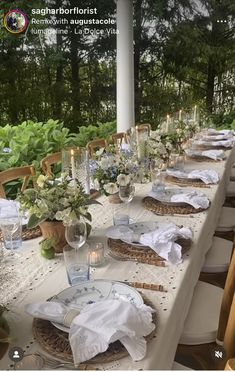 a long table is set with white linens and place settings for an outdoor dinner