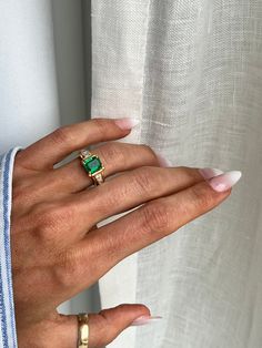 a woman's hand with two gold rings and an emerald ring on her finger