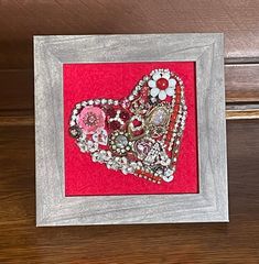 a heart made out of buttons and beads on a red background with a silver frame