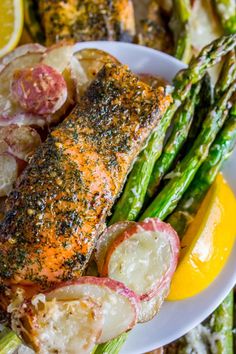 a white plate topped with fish and asparagus next to lemon wedged potatoes