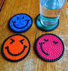 three smiley face coasters next to a glass of water on a wooden table top