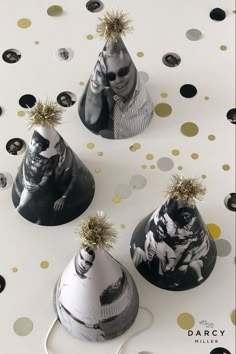 three black and white party hats with gold sprinkles on them, one has a man's face painted on it