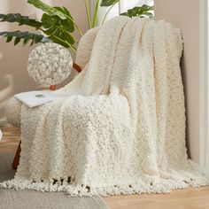 a white blanket sitting on top of a chair next to a potted plant