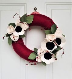 a red wreath with white and black flowers hanging on the front door, decorated with greenery