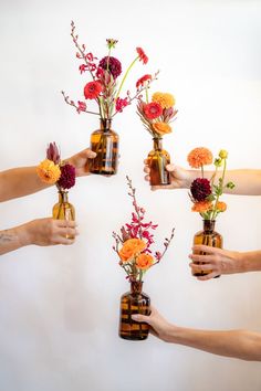 five arms holding warm-colored flowers in brown glass bud vases in front of a white background Dahlias Wedding, Gerber Daisy