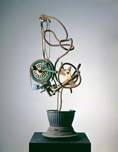 a sculpture made out of various items on top of a black stand with a white wall in the background