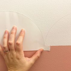 a person's hand on top of a piece of paper that has been taped to the wall