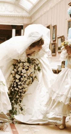 two women in white dresses and veils with flowers on the floor next to each other