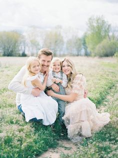 a man, woman and two children are sitting on the ground in an open field