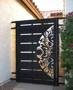 an iron gate in front of a house with flowers growing on the side and behind it