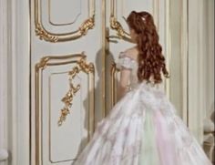 a woman in a white dress standing next to a door with gold trimmings