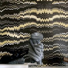 a vase sitting on top of a table next to a wallpaper covered in gold and black waves