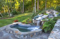 an outdoor hot tub in the middle of a yard with rocks and plants around it