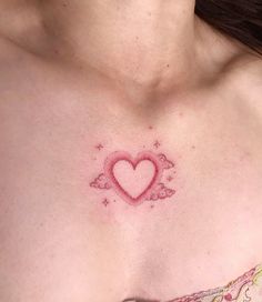 a woman's chest with a small heart tattoo on the chest and stars around it