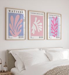 three framed posters above a bed in a room with white linens and neutral colors