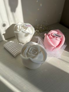 two white and pink roses sitting on top of a table next to each other in front of a window