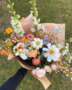 a person holding a bouquet of flowers in their hand on the grass with other flowers