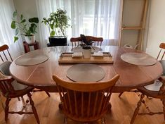 a wooden table with chairs around it in front of a window and potted plant