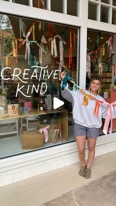 a woman standing in front of a store window holding up a sign that says creative kind