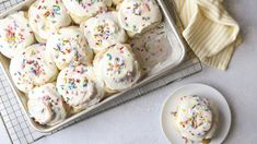 white frosted cookies with sprinkles on a cooling rack next to a plate