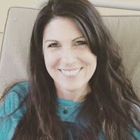 a woman with long hair sitting on a couch smiling at the camera and wearing a blue shirt