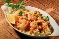 a white bowl filled with rice and shrimp on top of a wooden table next to a lemon wedge