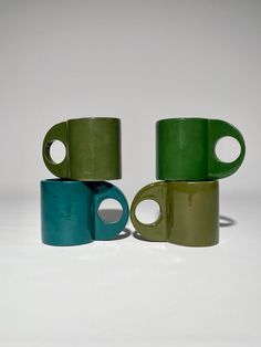 three green and one blue coffee mugs stacked on top of each other with holes in them